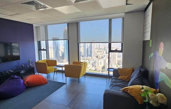 טרקלין משרדי מודרני עם פופים, כורסאות, ספה וטלוויזיה המותקנת על הקיר; חלונות גדולים המשקיפים על נוף העיר מתחם הבורסה רמת גן במגדל השחר.