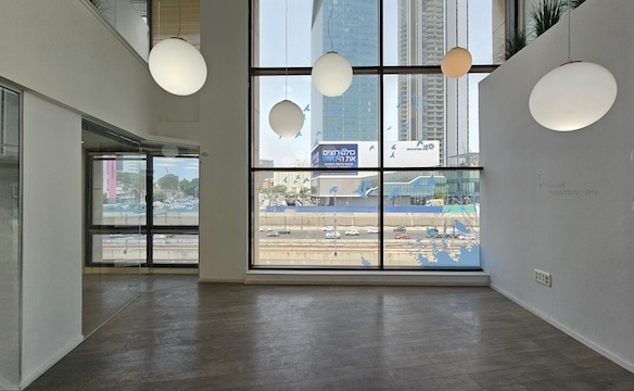 משרד להשכרה מודרני וריק בשטח של 450 מ"ר, עם חלונות מהרצפה עד התקרה, מנורות תלייה כדוריות ונוף מרהיב של בנייני העיר ורחוב אגיד רבד ההומה מתחת.