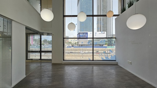 משרד להשכרה מודרני וריק בשטח של 450 מ"ר, עם חלונות מהרצפה עד התקרה, מנורות תלייה כדוריות ונוף מרהיב של בנייני העיר ורחוב אגיד רבד ההומה מתחת.