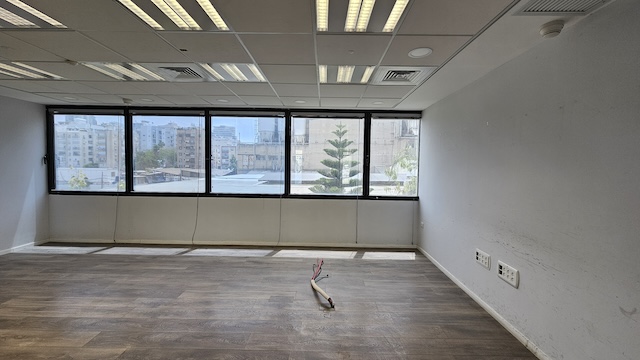 משרד להשכרה בגודל 450 מ"ר באגיד רבד, כולל חלל משרדי ריק עם חלונות גדולים, רצפת עץ, תאורה פלורסנטית, שקעי חשמל גלויים וחוטים חשמליים יוצאים מהרצפה.