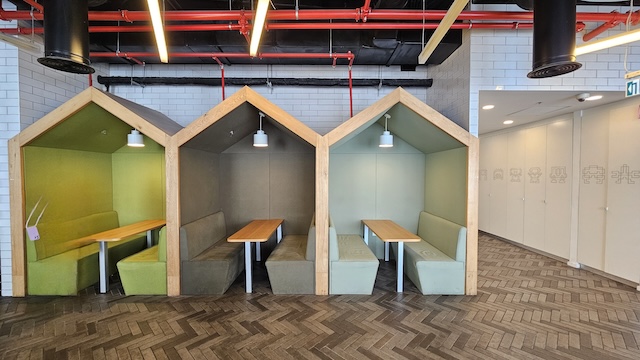 שלושה ספסלי ישיבה מעץ של Avantis, המעוצבים כבתים קטנים, מסודרים זה לצד זה בחדר מודרני ומואר היטב עם ריצוף אריחים בדוגמת אדרה בקומה 38 של מגדל אטריום.