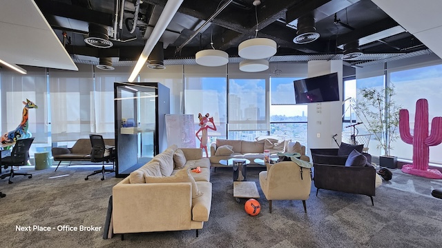 טרקלין משרדי מודרני למשרד להשכרה בבית קרדן, תל אביב, עם ספות בצבע בז', כריות מפוזרות, טלוויזיה, קישוטים משעשעים בצורת ג'ירפות וקקטוסים, חלונות גדולים ונוף עוצר נשימה של העיר.