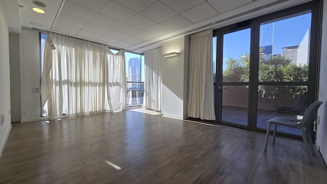 משרד מואר וריק עם ריצוף עץ, חלונות גדולים עם וילונות שקופים וכיסא פלסטיק בודד ליד דלת זכוכית המובילה למרפסת ענקית במתחם הבורסה.