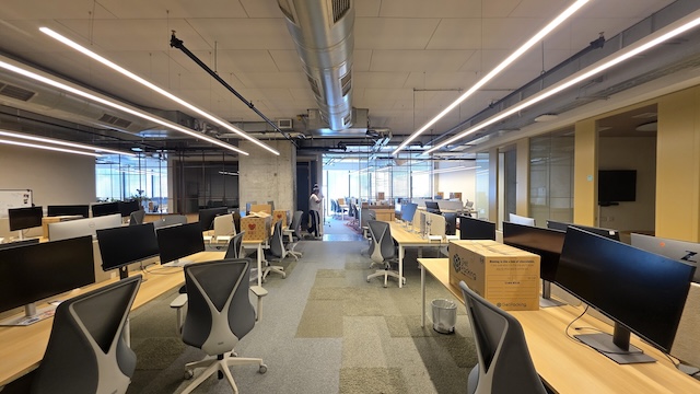 משרד יוקרתי להשכרה במגדלי דה וינצ'י, תל אביב, בעל עיצוב מודרני ופתוח, עם שורות של שולחנות ריקים, כיסאות משרדיים אלגנטיים, מסכים, ארגזים להובלה וחלונות גדולים הממלאים את החלל באור טבעי.