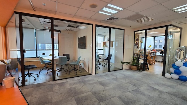 שטח משרדי מודרני להשכרה במתחם הבורסה, הכולל שלושה חדרי ישיבות עם קירות זכוכית, כיסאות ושולחנות; מימין ניתן לראות חלל עבודה פתוח עם שולחנות, ציוד וקבוצת בלונים כחולים.