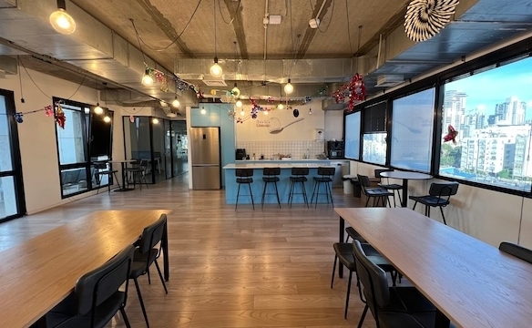 מטבח ומרחב אוכל מודרניים במשרד עם רצפות עץ, שולחנות, כיסאות, כסאות בר, חלונות גדולים, קישוטים חגיגיים, נוף לעיר ברקע ומרפסת המשקיפה על יגאל אלון.