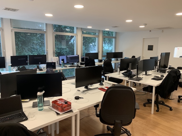 משרד מודרני עם מספר שולחנות ריקים, מחשבים, כיסאות וחפצים אישיים; חלונות גדולים מספקים אור טבעי ונוף לעצים בחוץ. משרד להשכרה ברחוב החשמונאים תל אביב.