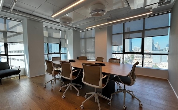 חדר ישיבות מודרני עם שולחן ארוך המוקף בשמונה כיסאות, חלונות גדולים, רצפת עץ ונוף לעיר – אידיאלי לישיבות בבית ישראכרט ומושלם למי שמחפש משרד מודרני להשכרה.