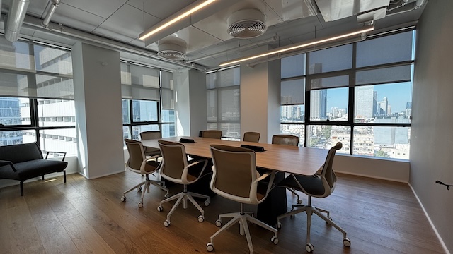 חדר ישיבות מודרני עם שולחן ארוך המוקף בשמונה כיסאות, חלונות גדולים, רצפת עץ ונוף לעיר – אידיאלי לישיבות בבית ישראכרט ומושלם למי שמחפש משרד מודרני להשכרה.