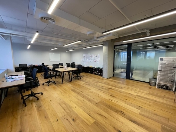 משרד מודרני עם רצפות עץ, מספר שולחנות וכסאות ריקים, לוח לבן, ציורים על הקירות וחדר ישיבות עם קירות זכוכית במתחם הבורסה בבית אבגד. משרד גדול להשכרה המתאים לעסקים מכל התחומים.