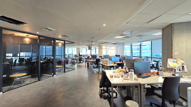 משרד מודרני בעל חלל פתוח עם מספר שולחנות, מחשבים וכסאות בבית שאפ, מתחם הבורסה רמת גן. חדרי ישיבות מזכוכית נראים משמאל; חלונות גדולים מקיפים את הקיר הרחוק. המשרד להשכרה נראה ריק.