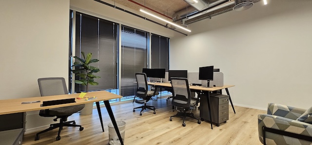 משרד להשכרה בעזריאלי טאון תל אביב עם מספר שולחנות, כיסאות, מסכי מחשב וצמח. בחלל רצפת עץ בהירה, תריסים על חלונות גדולים ועיצוב מינימליסטי.