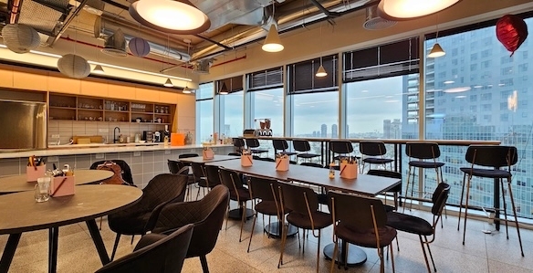 מטבח משרדי מודרני ופינת אוכל עם שולחנות, כיסאות, מקומות ישיבה ליד חלונות גדולים ונוף מרהיב של קו הרקיע של תל אביב ועזריאלי טאון. משרד להשכרה מושלם לצוותים המחפשים סגנון ונוחות.