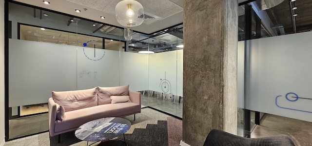 חלל משרדים מודרני מסוג Plug & Play עם ספה ורודה, שולחן עגול וקירות זכוכית חלבית עם עיצובים כחולים מינימליסטיים בעמינדב תל אביב. עמוד בטון גדול ניצב במרכז החדר.